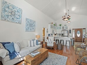 A spacious living room with a sofa, coffee table, and chairs, a kitchen with cabinets and appliances, and a dining area with stools.