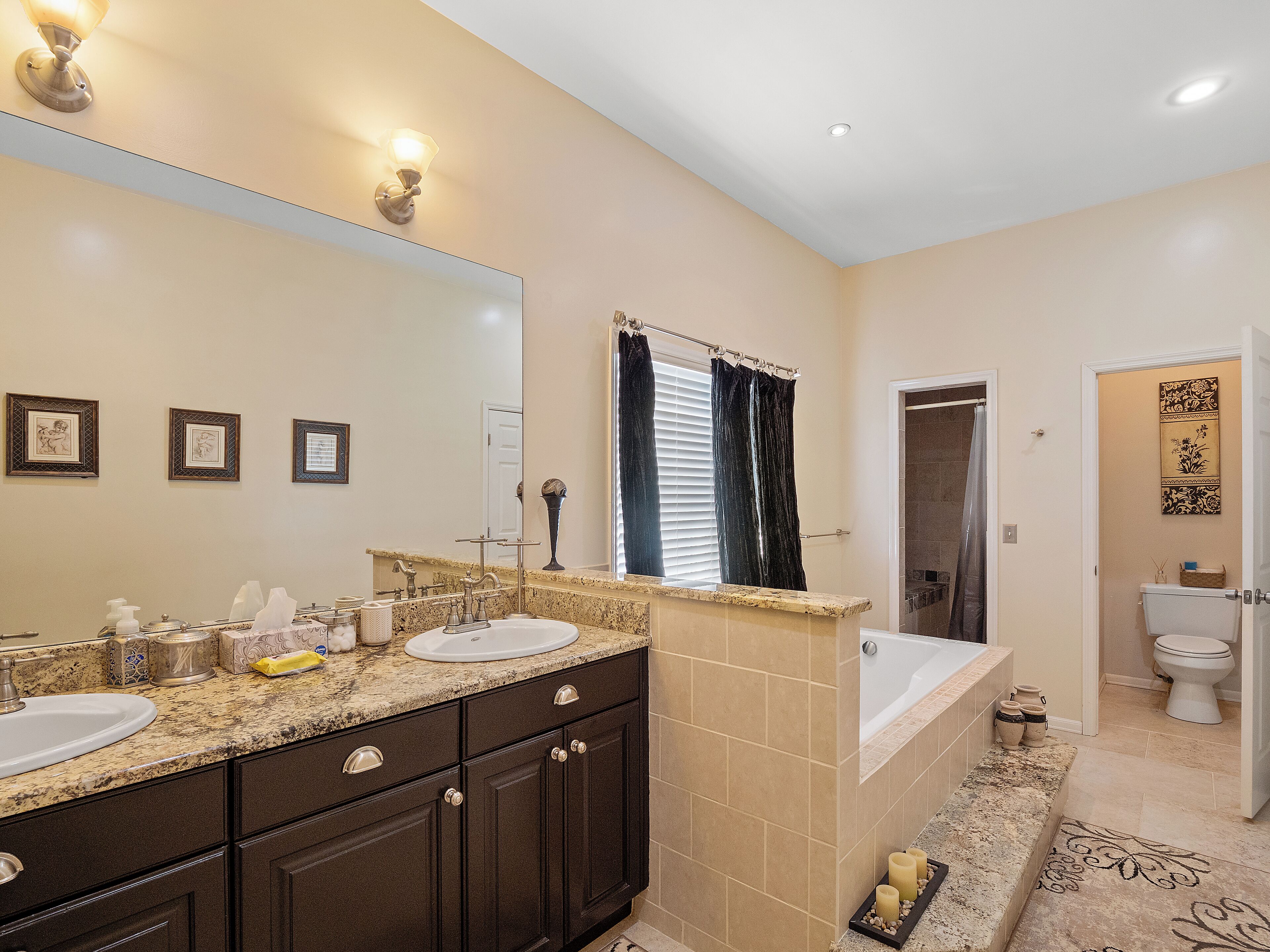 A bathroom with a double sink vanity, a large mirror, a bathtub, and a toilet.