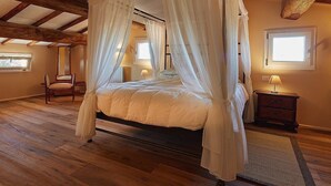 Un lit à baldaquin à quatre poteaux dans une pièce dotée de poutres en bois, d’un plancher en bois et d’une fenêtre laissant entrer la lumière naturelle.