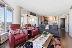Un salon moderne avec un canapé en cuir rouge, un divan gris et une table à manger agrémentée d’un chemin de table à motifs floraux.