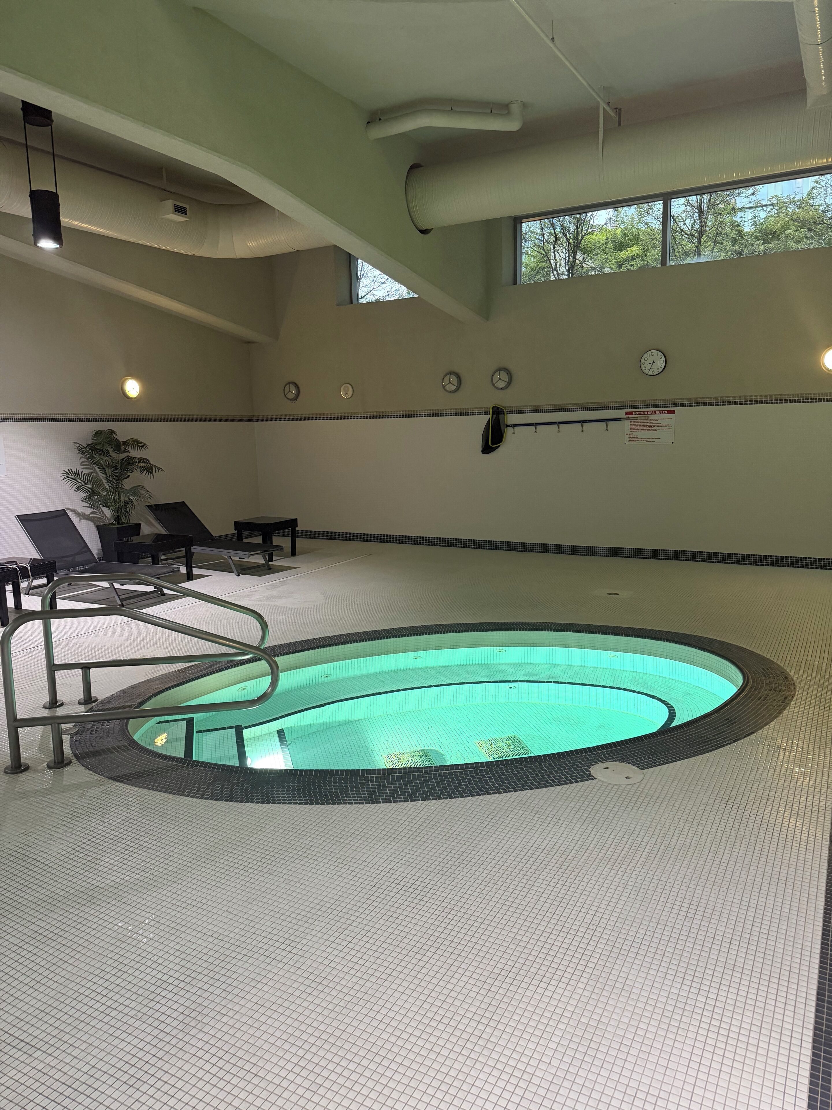 Une piscine avec une terrasse carrelée, des chaises longues et une horloge au mur.