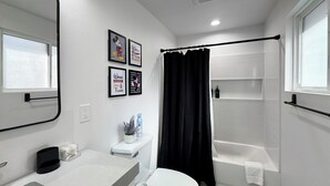 Un bagno moderno con toilette, lavabo e vasca da bagno. Alle pareti sono presenti quadri incorniciati e una tenda da doccia.