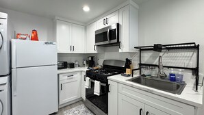 Una cucina moderna con mobili bianchi, un lavello in acciaio inossidabile, un forno a microonde e un piano cottura.