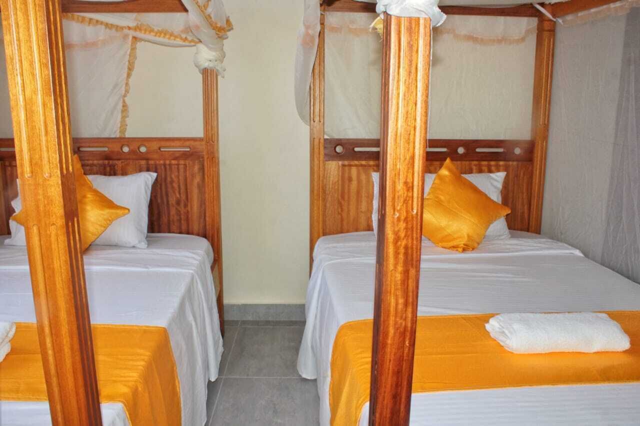 A room with two wooden four-poster beds, each with a white bedspread and a single yellow pillow.