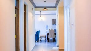 A hallway with a ceiling light fixture, a dining area with a table and chairs, and a door on the left. - Pavilion Suites Nyali (Mombasa)
