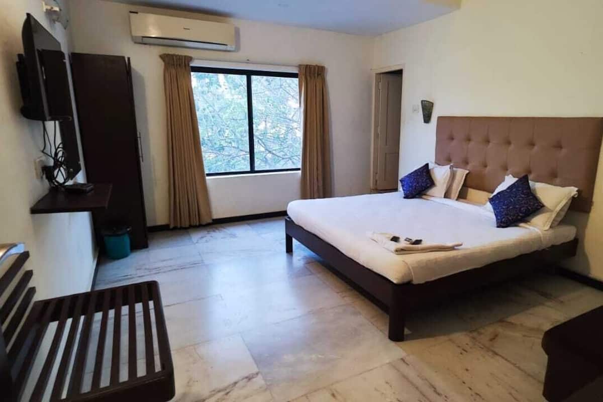 Ein Hotelzimmer mit einem großen Bett, einem an der Wand montierten Fernseher, einem Fenster mit Vorhängen und einer hölzernen Bank.
