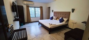 A hotel room with a large bed, a TV mounted on the wall, a window with curtains, and a wooden bench. - Stayz Inn Teynampet (Chennai)