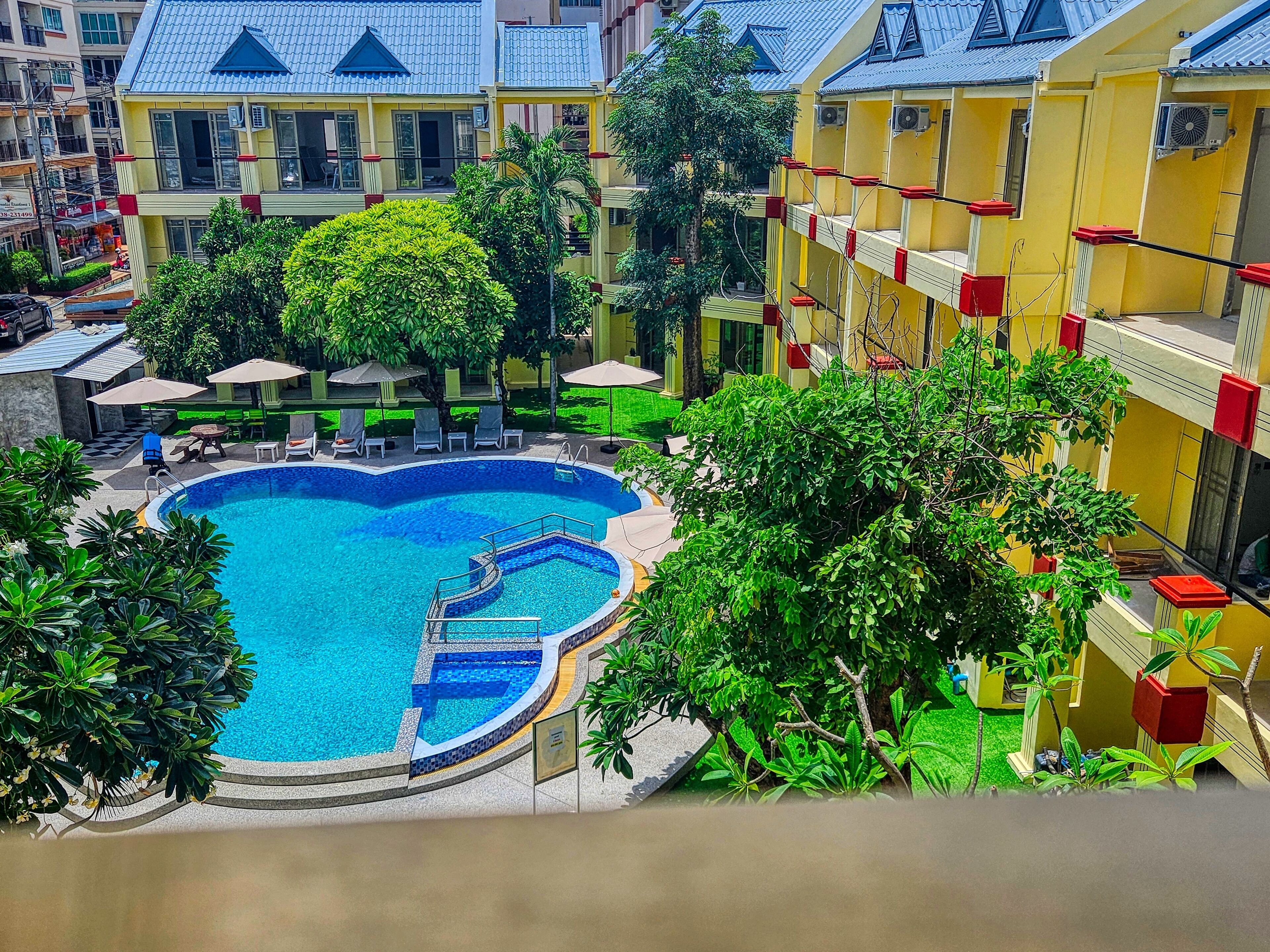 A swimming pool surrounded by lush greenery and yellow buildings with red accents.