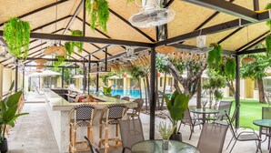 An outdoor dining area with a pool, covered seating, and hanging plants. - Mermaid Beach Resort - 100m to Beach, Saltwater Pool & BeerGarden (Pattaya)