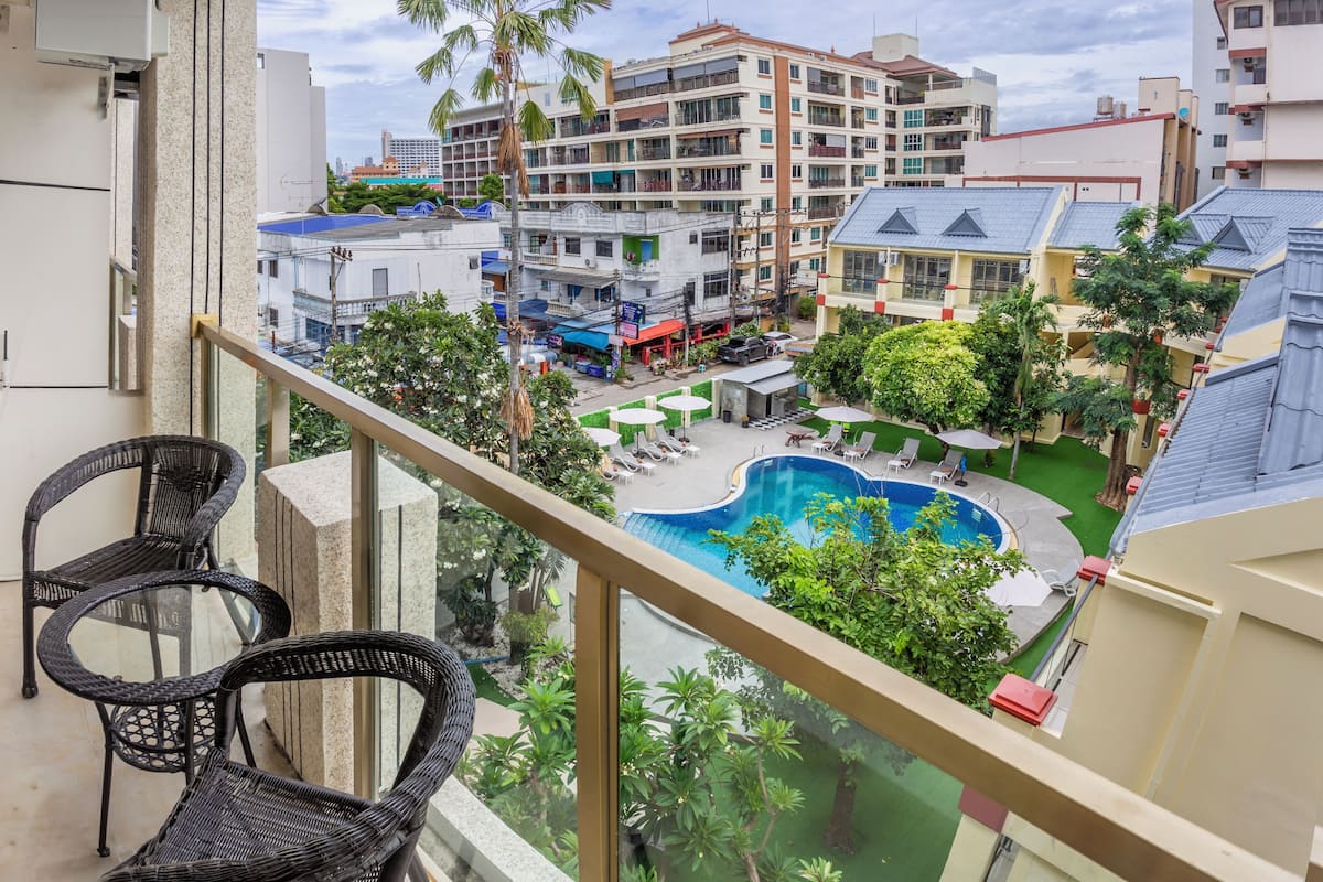 Un balcon doté de fauteuils en osier, donnant sur un espace piscine avec des chaises longues et un petit jardin.