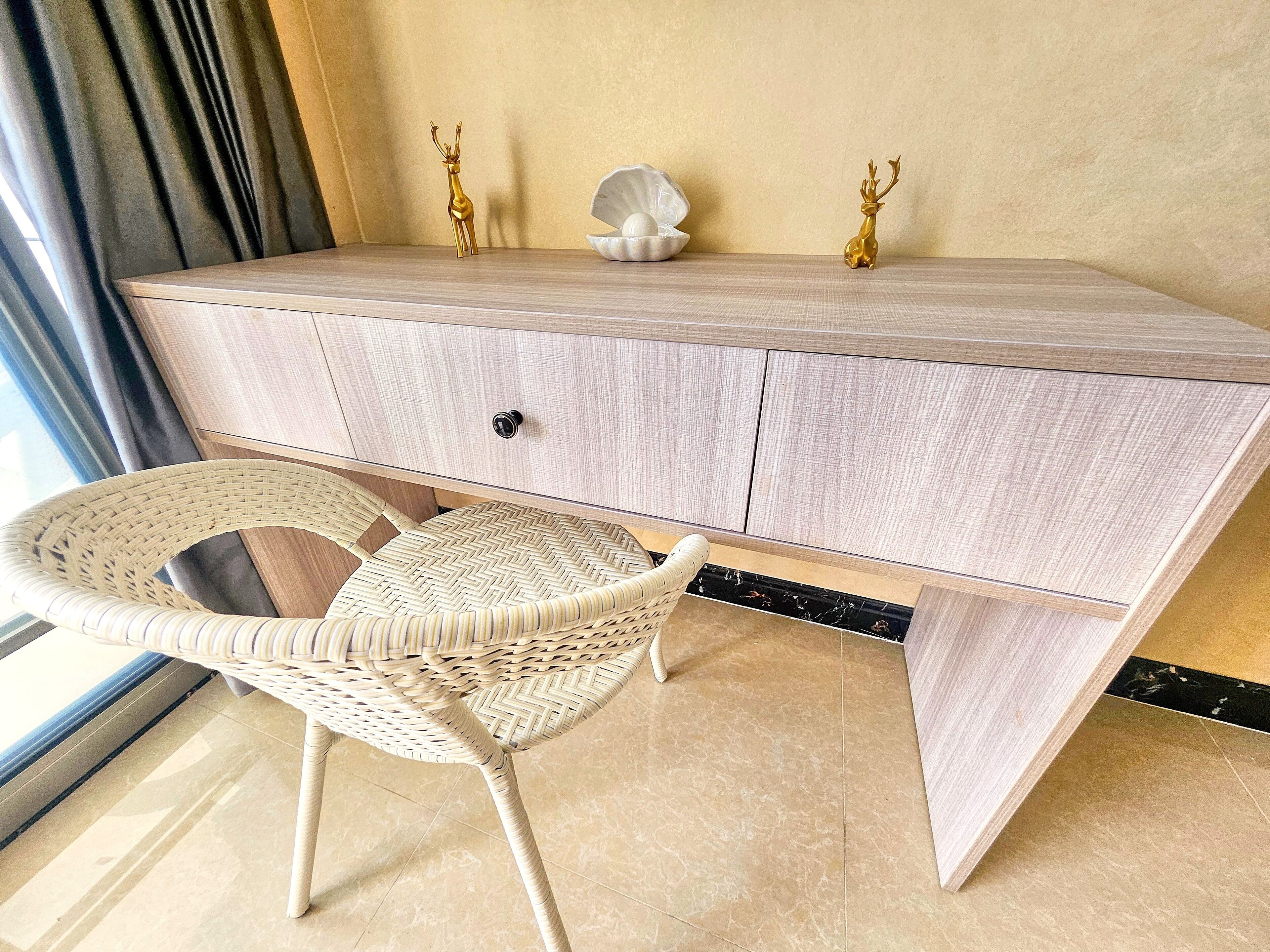 A modern desk with a light wood finish, a wicker chair, and decorative golden deer figurines.