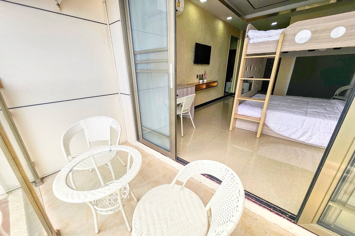 Une chambre d’hôtel avec un balcon, un lit, un bureau et deux fauteuils en osier.