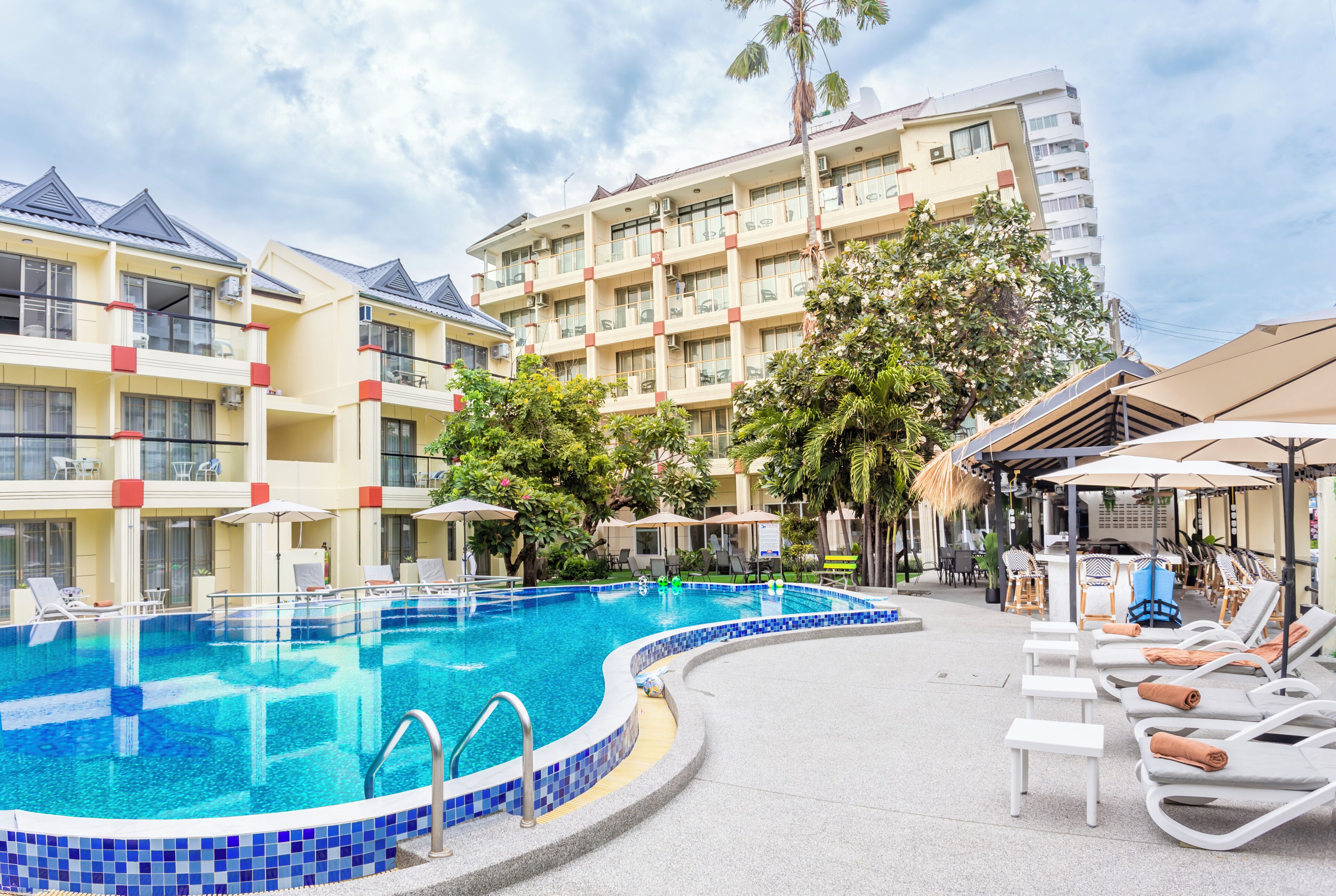 A hotel with a swimming pool, lounge chairs, and umbrellas.