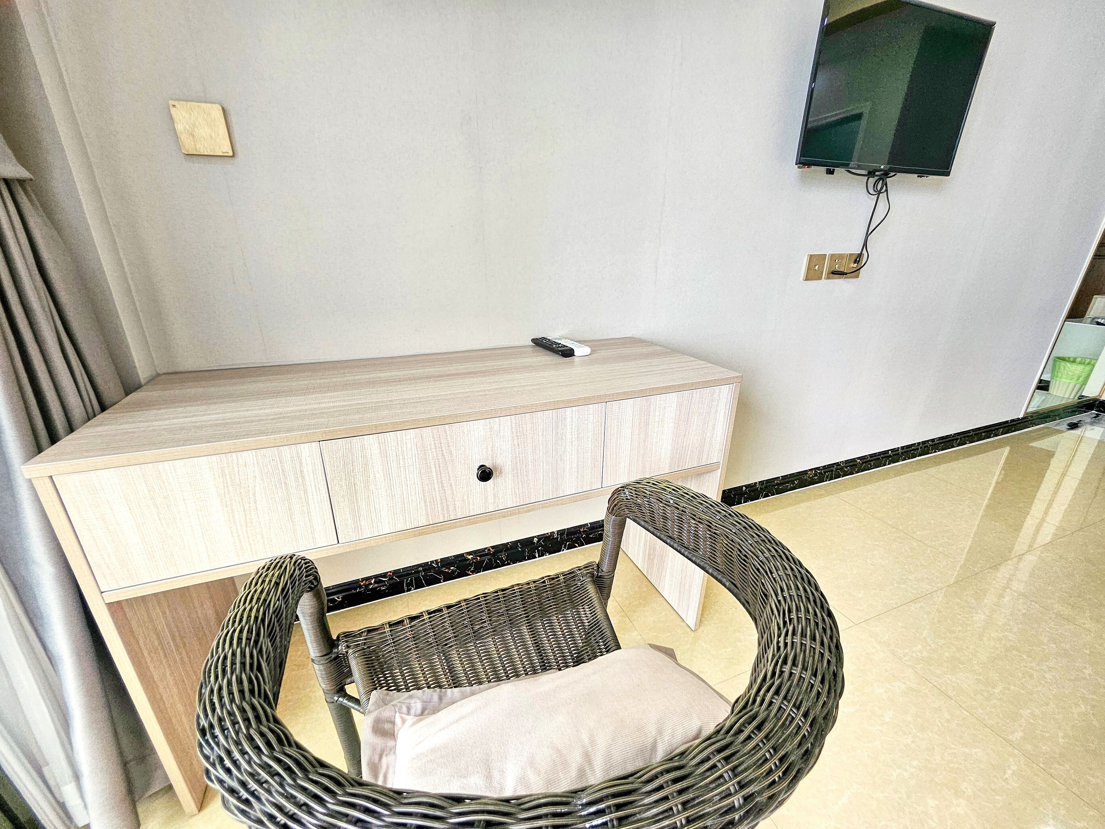 A room with a wooden desk, a wicker chair, and a flat-screen TV mounted on the wall.