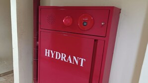 Een rode hydrant met de tekst 'HYDRANT', geplaatst in een hoek met betegelde vloer.