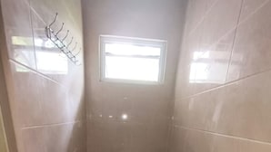 Een kleine, smalle badkamer met toilet, een raam en een douchegedeelte.