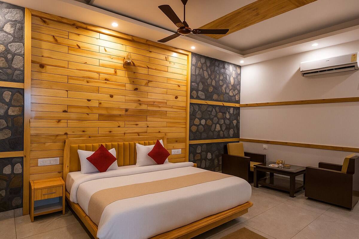Un dormitorio con cabecera de madera, cama con ropa de cama blanca y almohadas rojas, una mesita con una silla y un equipo de aire acondicionado en la pared.