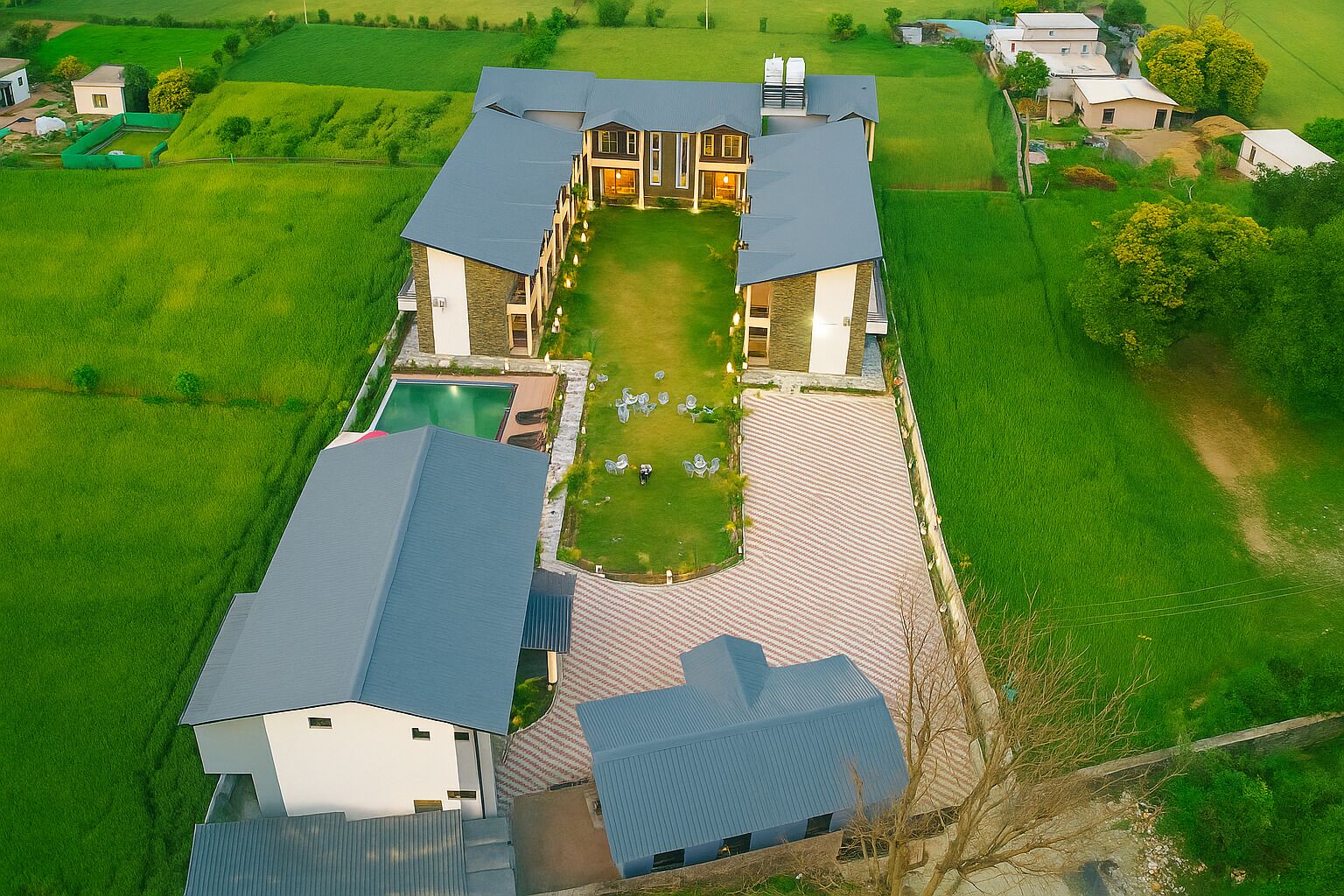 An aerial view of a large estate with a swimming pool, multiple buildings, and expansive green fields.
