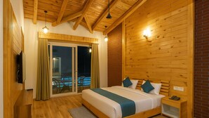 Ein Schlafzimmer mit Holzboden, einem Bett mit grüner und weißer Bettdecke, einem Nachttisch und einer Schiebetür zu einem Außenbereich.