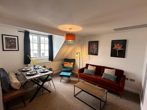 Uma sala de estar moderna com mesa de jantar, sofá vermelho e poltrona azul.