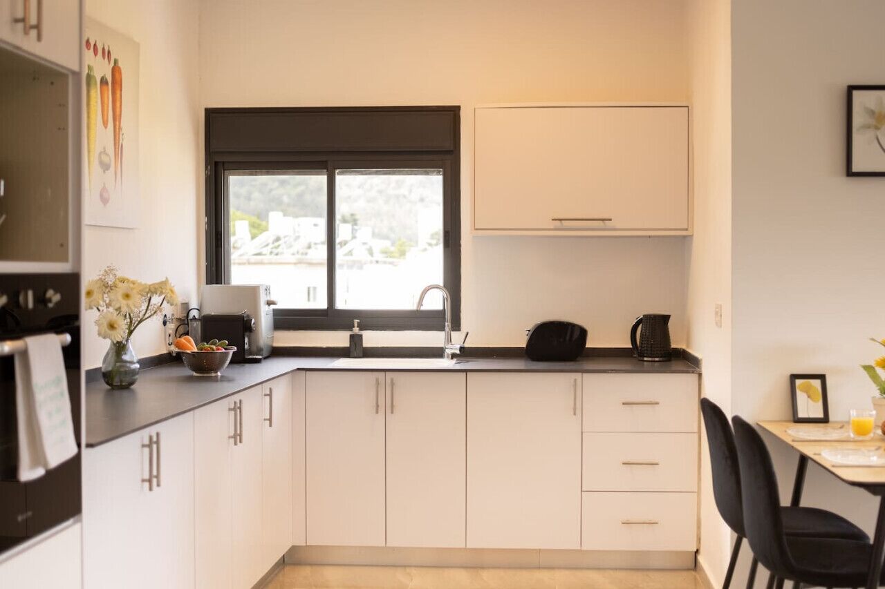 A compact kitchen with white cabinets, a black countertop, a sink, and a window.