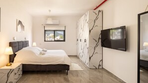 A modern bedroom with a bed, bedside tables, a wardrobe, a TV, and a window with a view. - MAMAD - Stella Maris views Vista apartments by Sea N' Rent (Haifa)