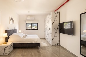 A bedroom with a bed, a TV, a wardrobe, a window, and a mirror. - MAMAD - Stella Maris views Vista apartments by Sea N' Rent (Haifa)
