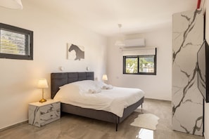 A bedroom with a bed, nightstand, lamp, window, and artwork.