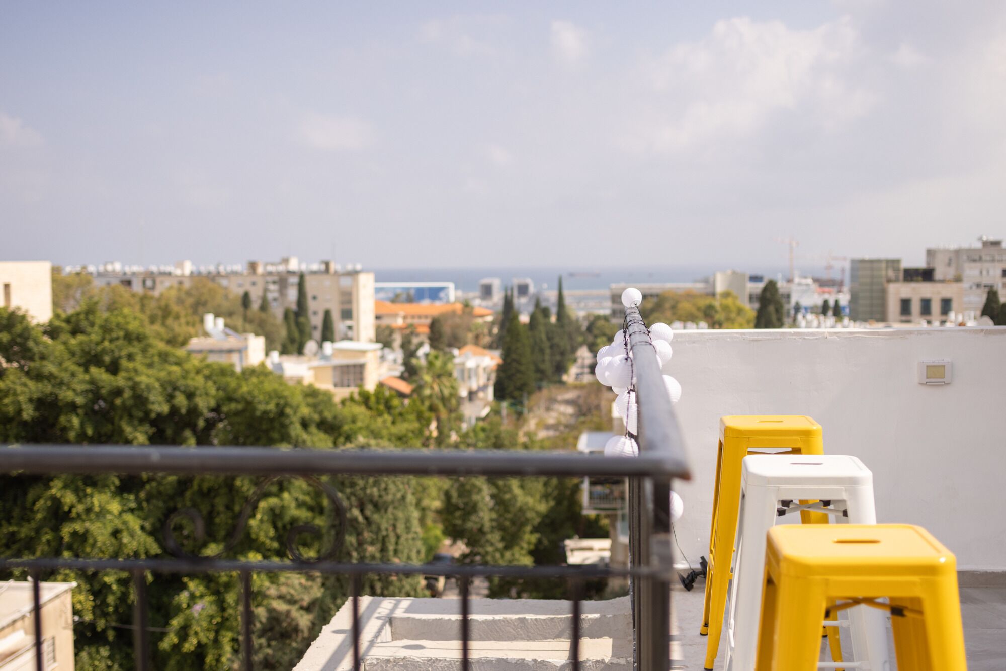 Eine Dachterrasse mit Geländer, einer Statue und gelb-weißen Hocker.