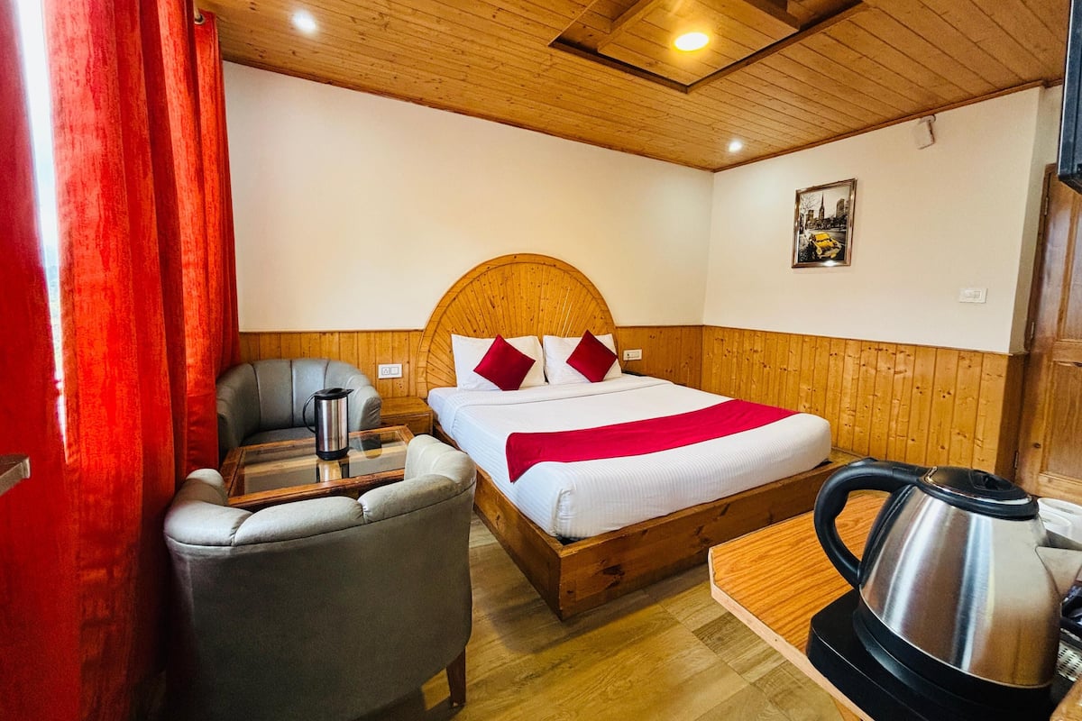 Una camera accogliente con un letto e una testiera in legno, una poltrona grigia, un tavolino con un bollitore e un quadro appeso al muro.