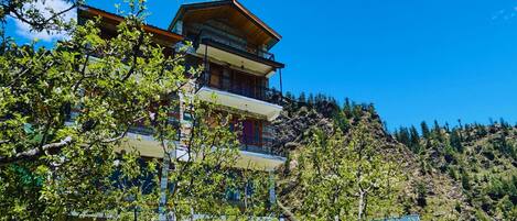 A multi-story building with a traditional architectural style, surrounded by trees and set against a mountainous backdrop.