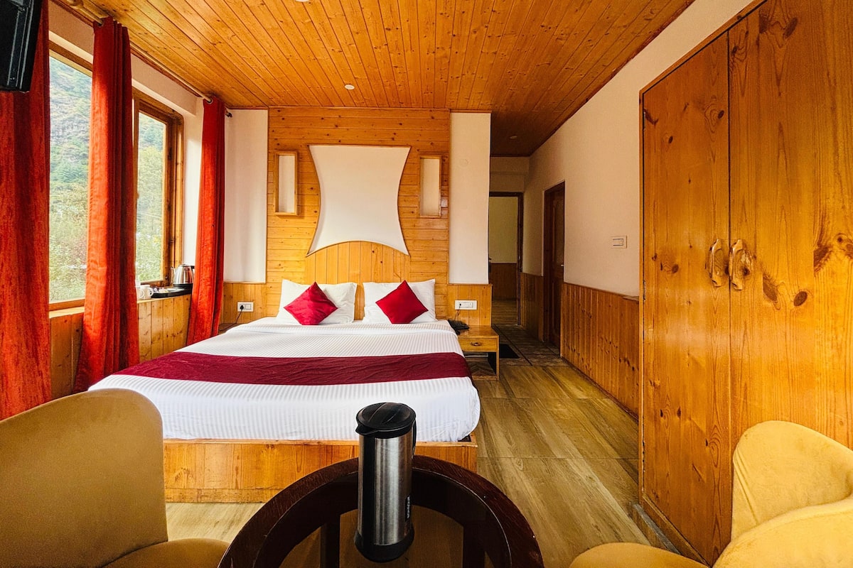 Camera da letto con rivestimento in legno, un letto grande, cuscini rossi, un comodino e vista sull'esterno.