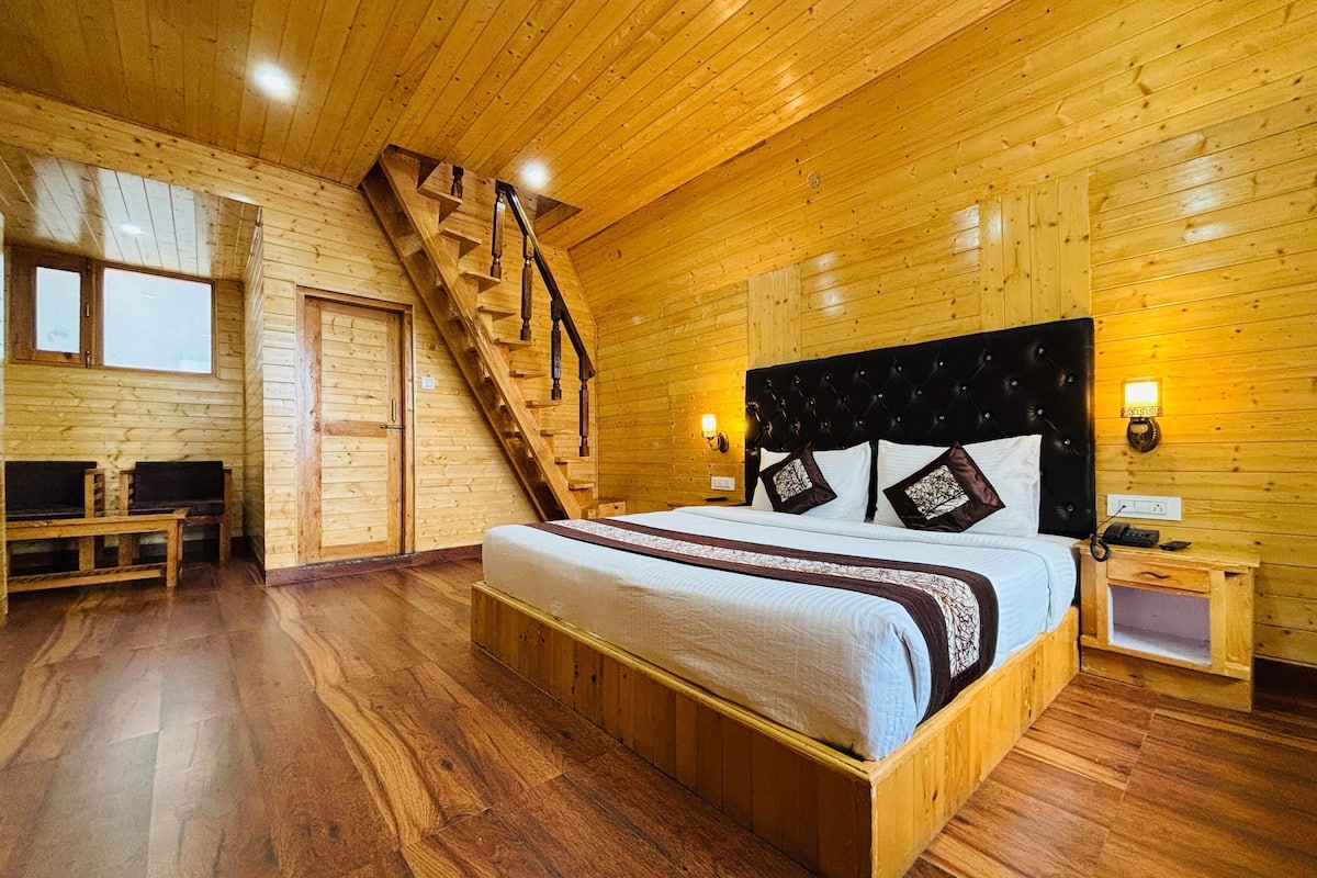 Camera da letto in una baita di legno, con un letto, una scala, una panca e un comodino.