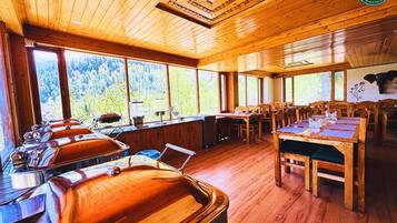 A wooden interior with large windows, a pool table, and multiple dining tables.