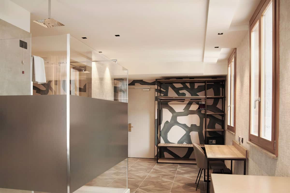 Une chambre d’hôtel moderne avec une cloison en verre, un bureau en bois et un mur décoré d’un motif.