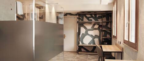 A modern hotel room with a glass partition, a wooden desk, and a patterned wall.