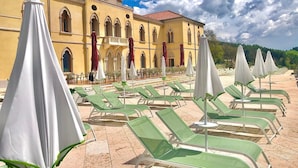 A hotel with a courtyard featuring green lounge chairs and white umbrellas, a yellow building with arched windows, and a clear blue sky. - Parc Hotel San Pietro  (Caprino Veronese)