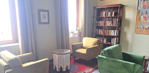 Una sala de estar con un sillón color crema, un sillón verde, una pequeña mesita blanca y una amplia estantería de madera.
