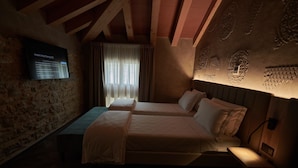A dimly lit room with two beds, a stone wall, and a mounted screen displaying text. - Parc Hotel San Pietro  (Caprino Veronese)