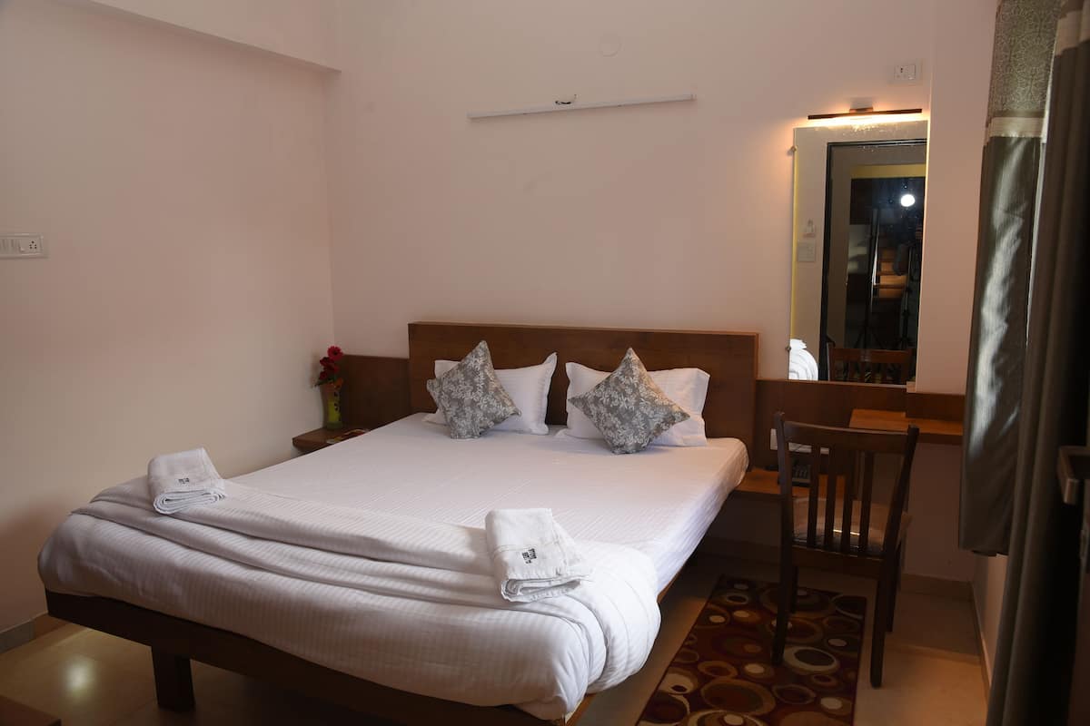 A neatly made bed with pillows, a wooden headboard, a small table with a chair, and a mirror on the wall.
