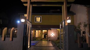 A gated entrance to a building at night with illuminated pathways and a pool area visible. - Stone Shelter (Mahabaleshwar)