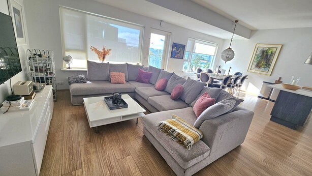 Ein modernes Wohnzimmer mit einem grauen Ecksofa, einem weißen Couchtisch und einem Essbereich mit rundem Tisch und Stühlen.