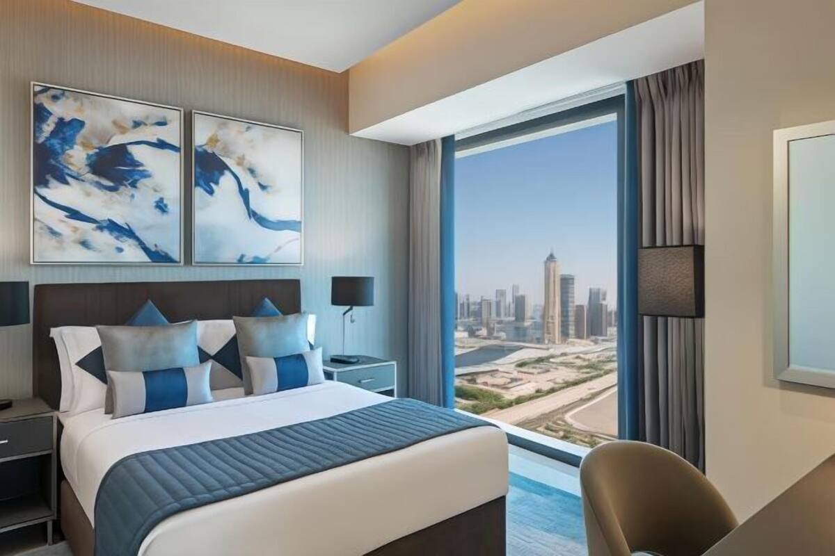 A modern hotel room with a large bed, a desk, and a view of a cityscape.