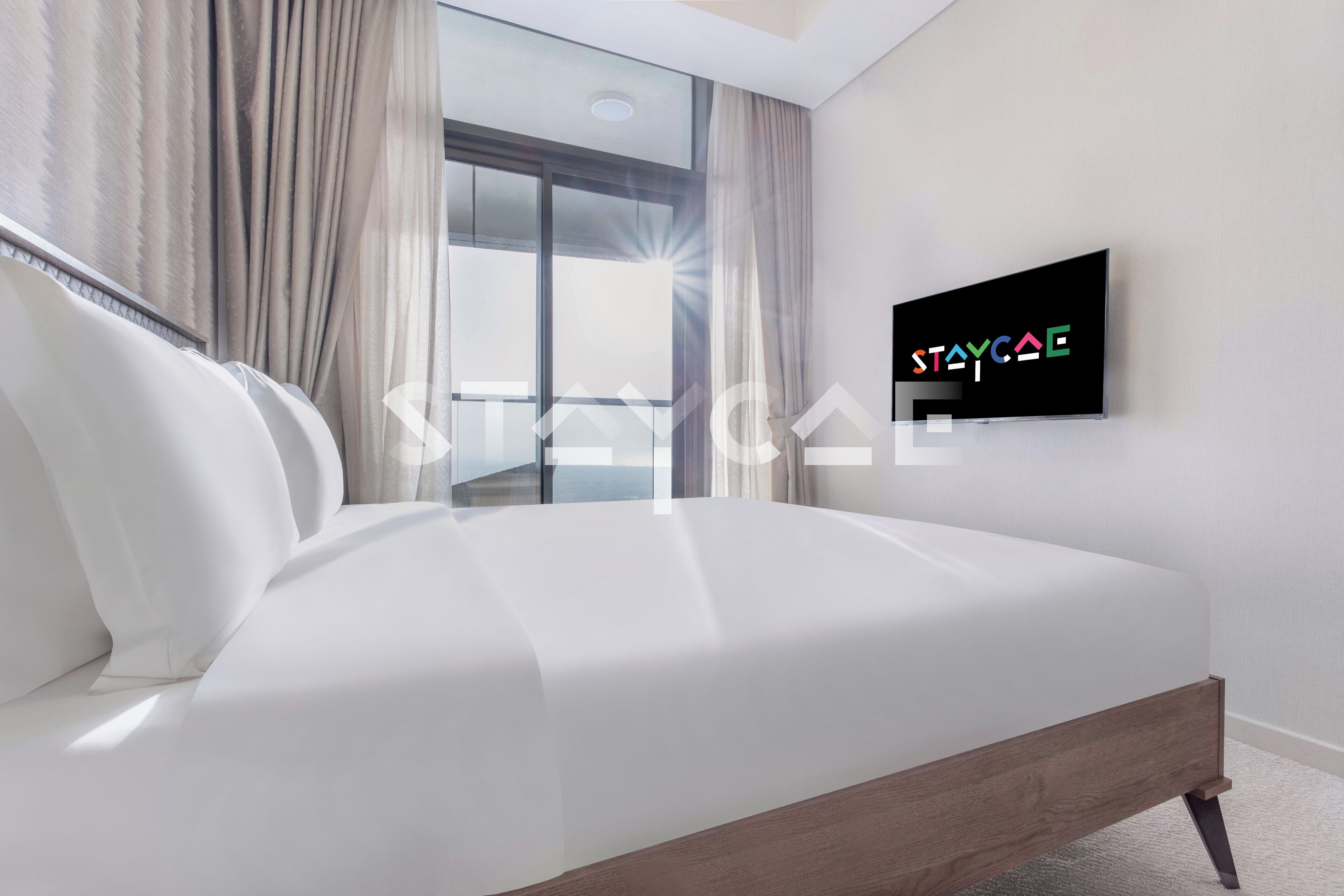 A modern bedroom with a large bed, a TV mounted on the wall, and a view of the outdoors through a large window.