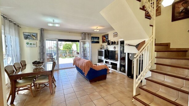 Amplia sala de estar con mesa y sillas de comedor, un sofá, una escalera y un televisor.
