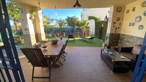 Un patio al aire libre con una mesa y sillas de madera, una tumbona y una zona de estar con cojines.