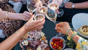 Un groupe de personnes trinquant avec des coupes de champagne lors d’une réception en plein air, devant une planche de charcuterie et du pain.
