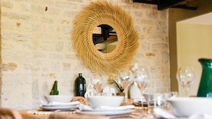 Une table à manger dressée avec de l’assiette, des bols et des verres blancs, et une tapisserie murale tissée au-dessus.
