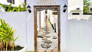 Un sendero conduce a Bukawa Residence, con un muro blanco y un cartel sobre la entrada.