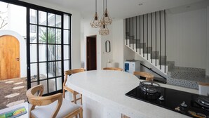 Una cocina moderna con una isla grande, sillas de madera, una estufa negra y una escalera que sube a un altillo.